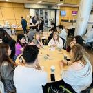 Groups of students sit around round tables working on crafts together.