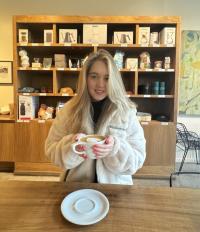 Photograph of Ameliya Davydova seated in a coffee shop holding a cappuccino.