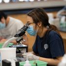 students wear masks and look through microscopes in a lab 