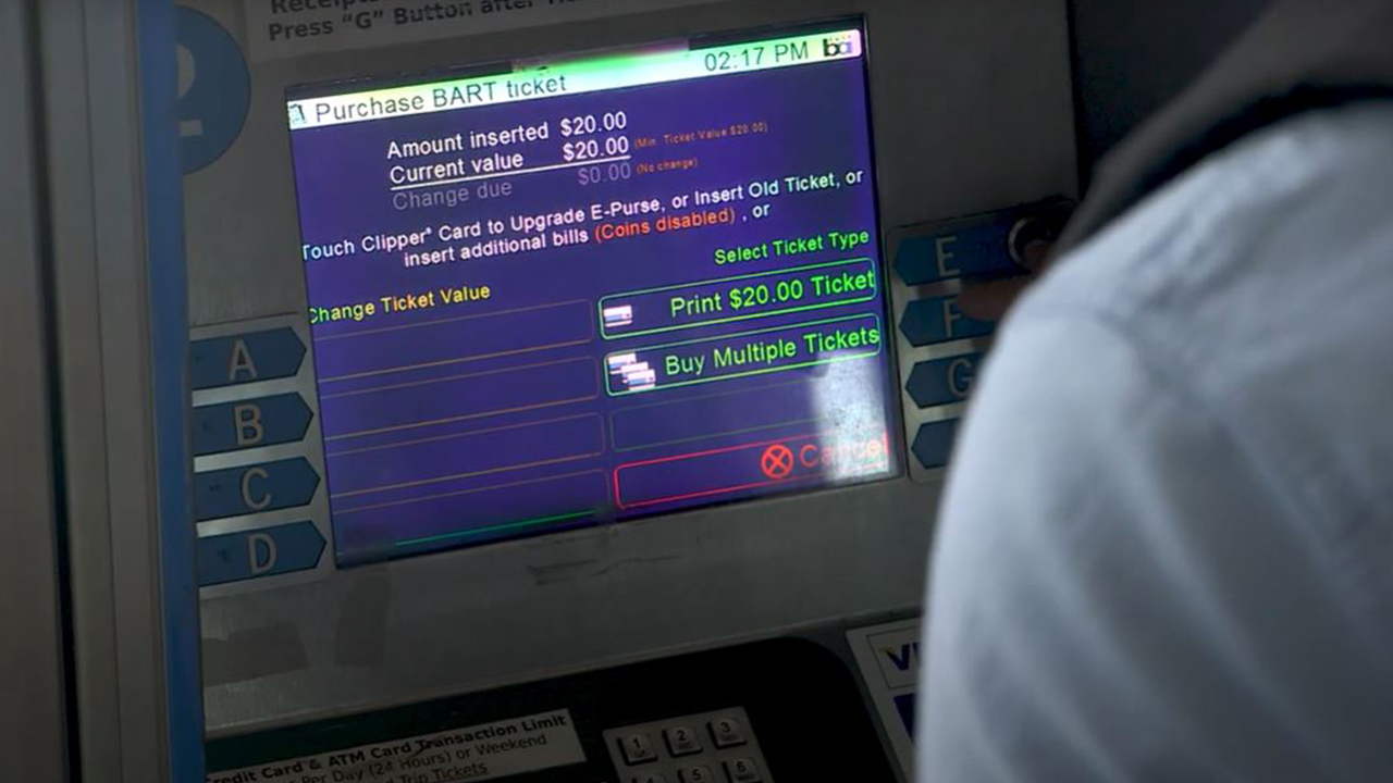 A traveler uses a payment kiosk at a BART station. The payment screen is displayed indicating that the traveler has added $20 to their fare. 