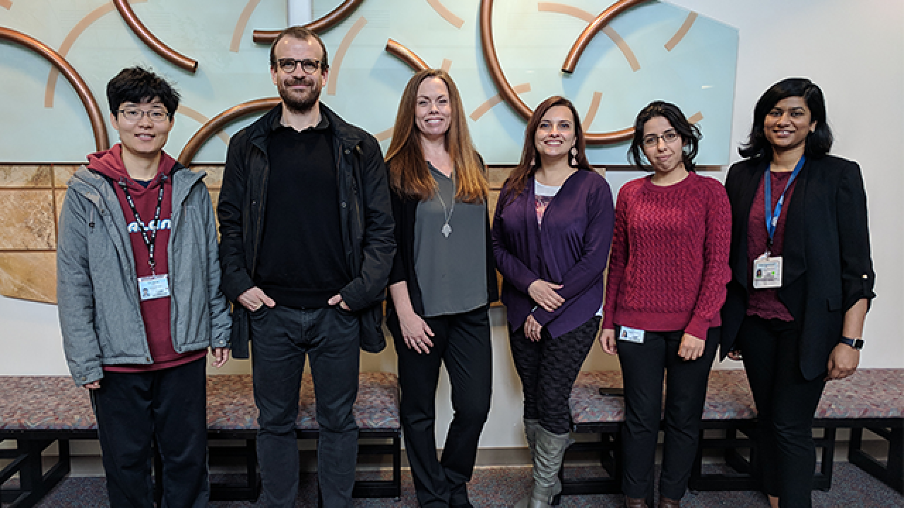 Jennifer Aten (center) with a few of the international scholars she has helped bring to the UC Davis Department of Neurology. group of adults standing in front of artwork