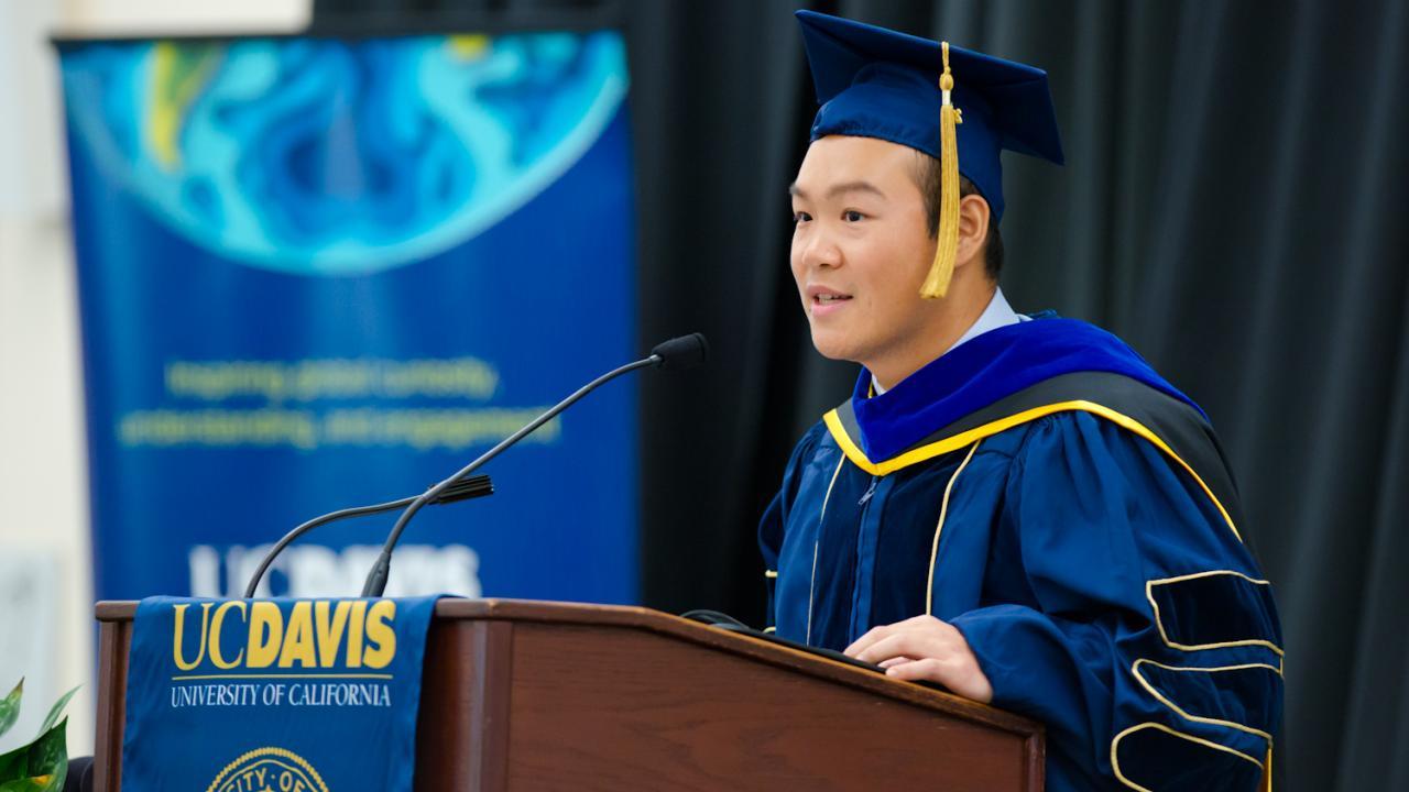 man in graduation cap speaking at podium 