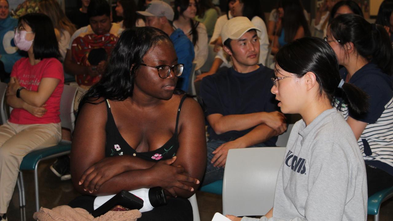 Two students talk to each other and are surrounded by other pairs of students.