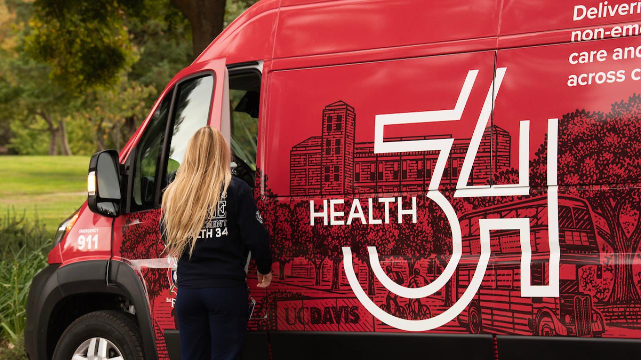 A woman opens the door of a red van that has "Health 34" printed on the side.