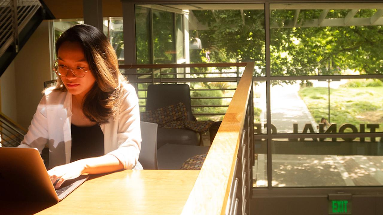 A student sits at a table and works on a labtop.