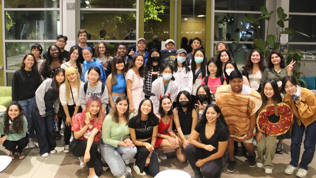 A group of students gather for a group photo, some in Halloween costumes, some in casual street clothes.