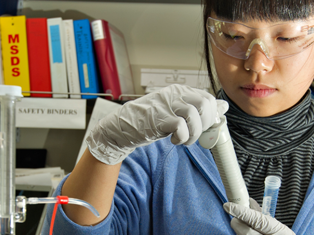 A person wears safety glasses and a lab coat and works with a pipet in a lab setting.