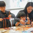 Two children build structures with kinex toys, their mother helps the youngest.