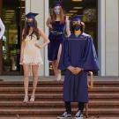 Six students wear commencement regalia and stand socially distanced wearing face masks on the steps of Mrak Hall on the UC Davis campus.