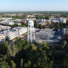 Aerial photograph of UC Davis campus taken on a sunny, clear morning from the south side of campus looking north with the UC Davis Water Tower in the front and Mrak Hall to the right. Campus buildings are visible through tree tops throughout the expanse of the campus, with the valley in the horizon.