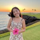 Photo of Cameron Lee holding a pink hibiscus overlooking a Hawiian beach at sunset.