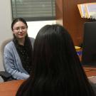 Stephanie sits in an office across the desk from a student whose back is to the camera as she listens.