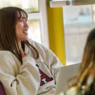 Smiling female student in sunlit classroom, white sweatshirt with letter A, purple chair