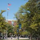 From the UC Davis Quad looking back at the Memorial Union on a sunny day, the USA and California state flags fly high in line with the tall trees in the area.