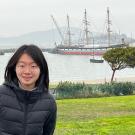 Photo of Chuyuan Wang with the ocean and a ship behind her.