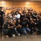 A group of 20 mentors from the Global Ambassador Mentorship Program pose inside the lobby of the UC Davis International Center. Fourteen students (four men and ten women) stand in a row at the back, and six women kneel in the front row. They hold small pumpkins and are dressed for fall weather.