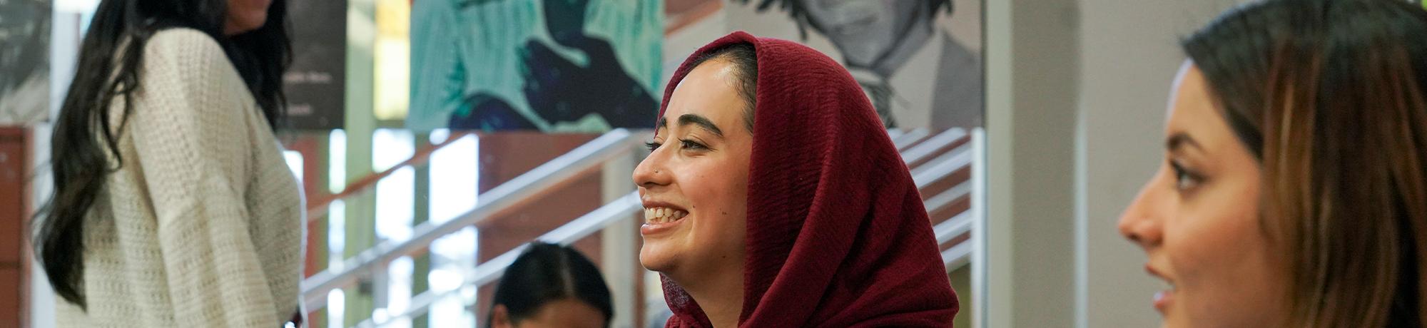 Two students in profile, one wears a headscarf and smiles.